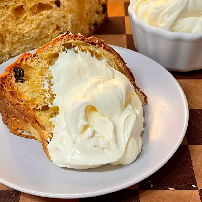 Fetta di Pandoro servita con una generosa cucchiaiata di crema al mascarpone pastorizzata.