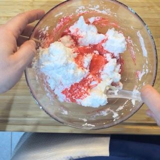 Una persona tiene in mano una ciotola di panna montata e salsa di fragole