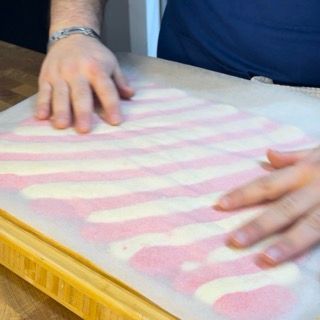 Una persona sta spalmando glassa rosa e bianca su un tagliere.