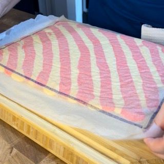 Una persona tiene in mano un pezzo di tessuto a strisce rosa e gialle su un tagliere di legno.