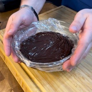 Una persona tiene in mano una ciotola di cioccolato ricoperta di pellicola trasparente