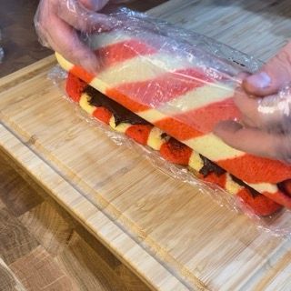 Una persona sta avvolgendo un panino nella pellicola trasparente su un tagliere di legno.