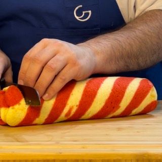 Un uomo con un grembiule blu sta tagliando un oggetto a strisce rosse e gialle