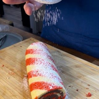 Una persona sta cospargendo di zucchero a velo un rotolo di bastoncino di zucchero