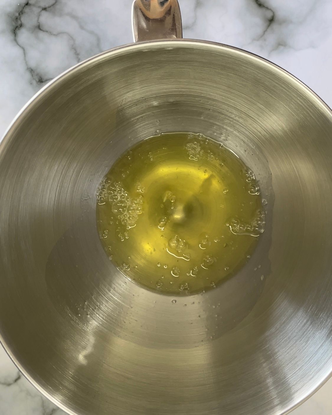 Una ciotola di metallo piena di un liquido giallo su un tavolo.