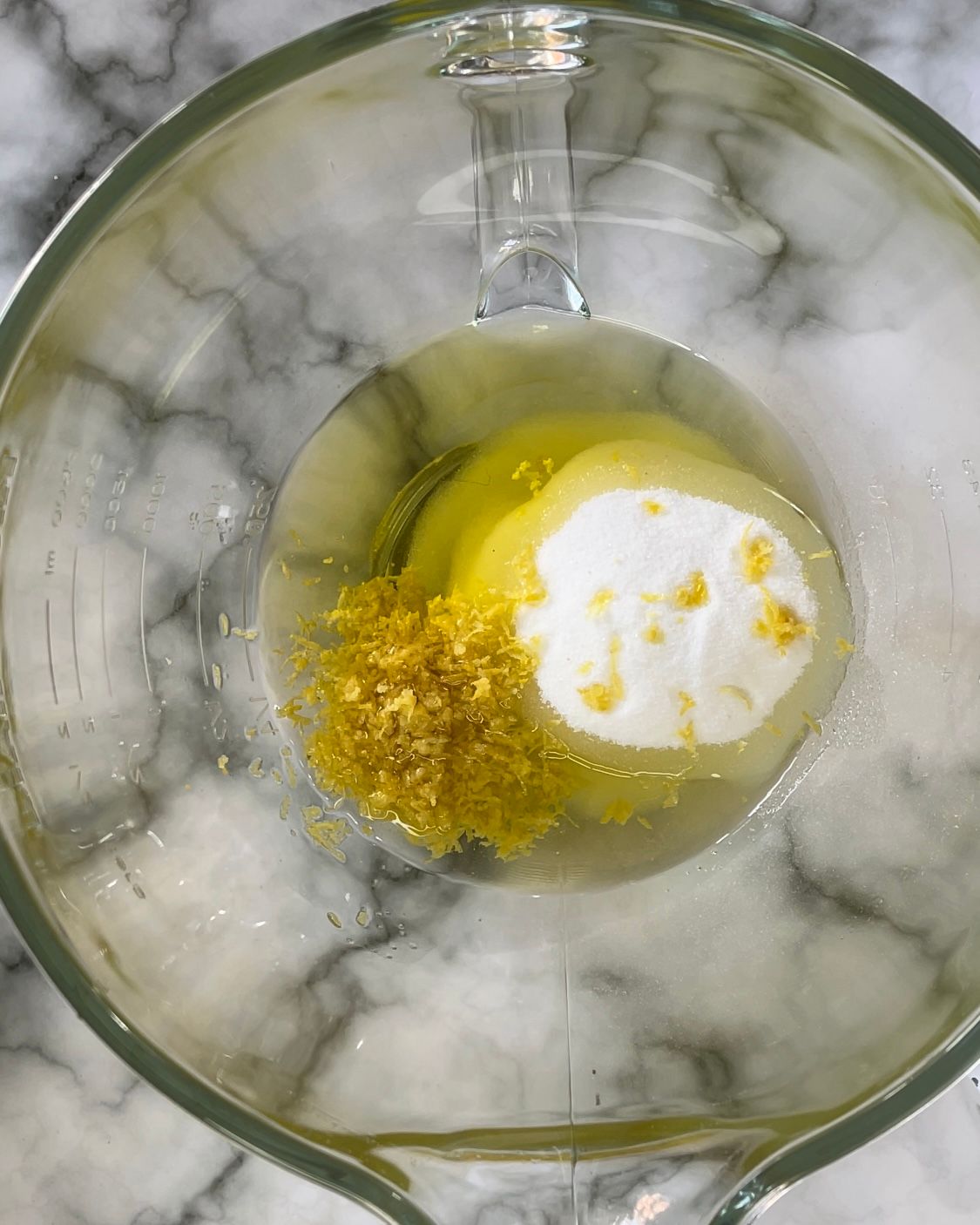 Una ciotola di vetro piena di uova, scorza di limone e bicarbonato di sodio.