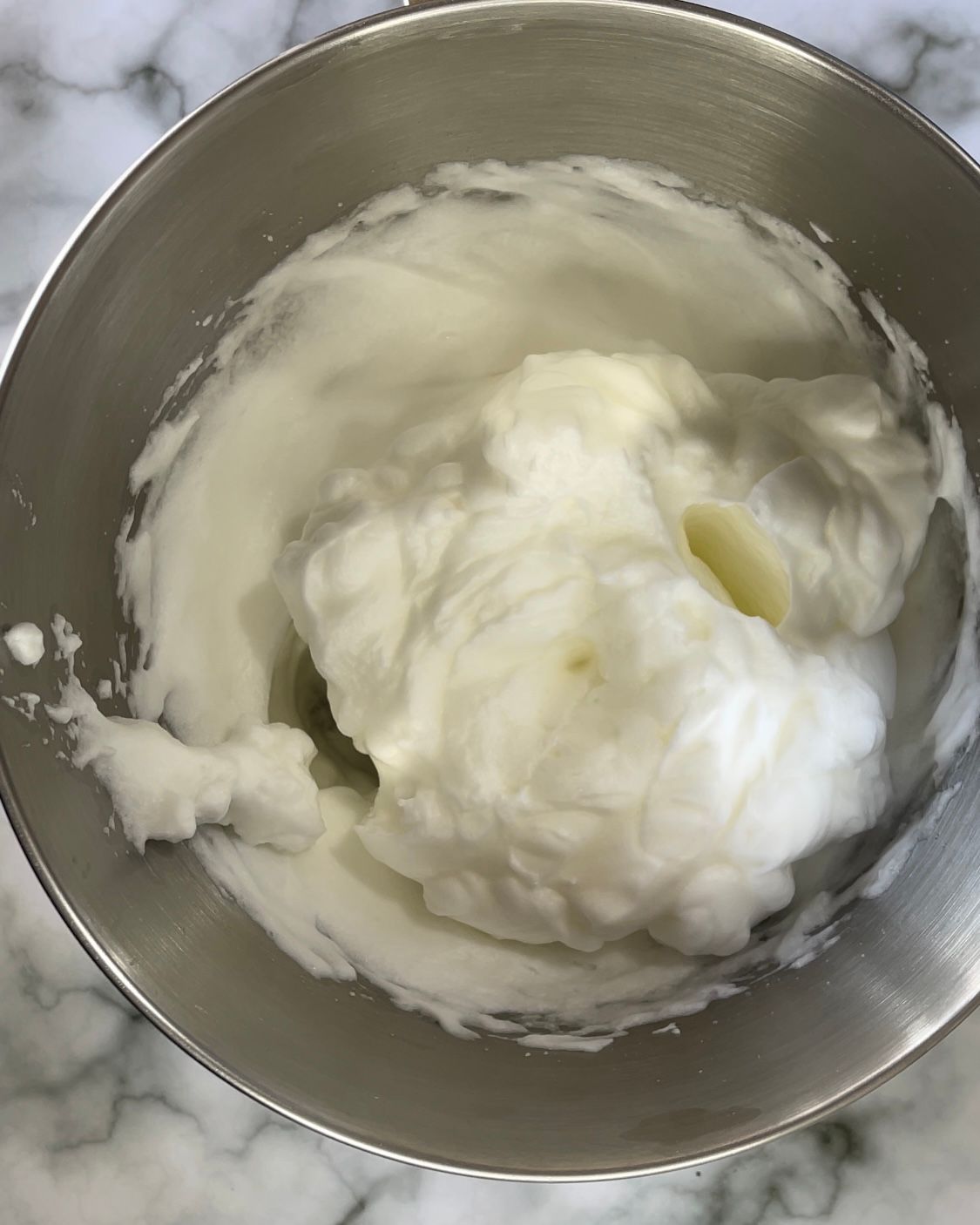 Una ciotola di metallo piena di panna montata su una superficie di marmo.