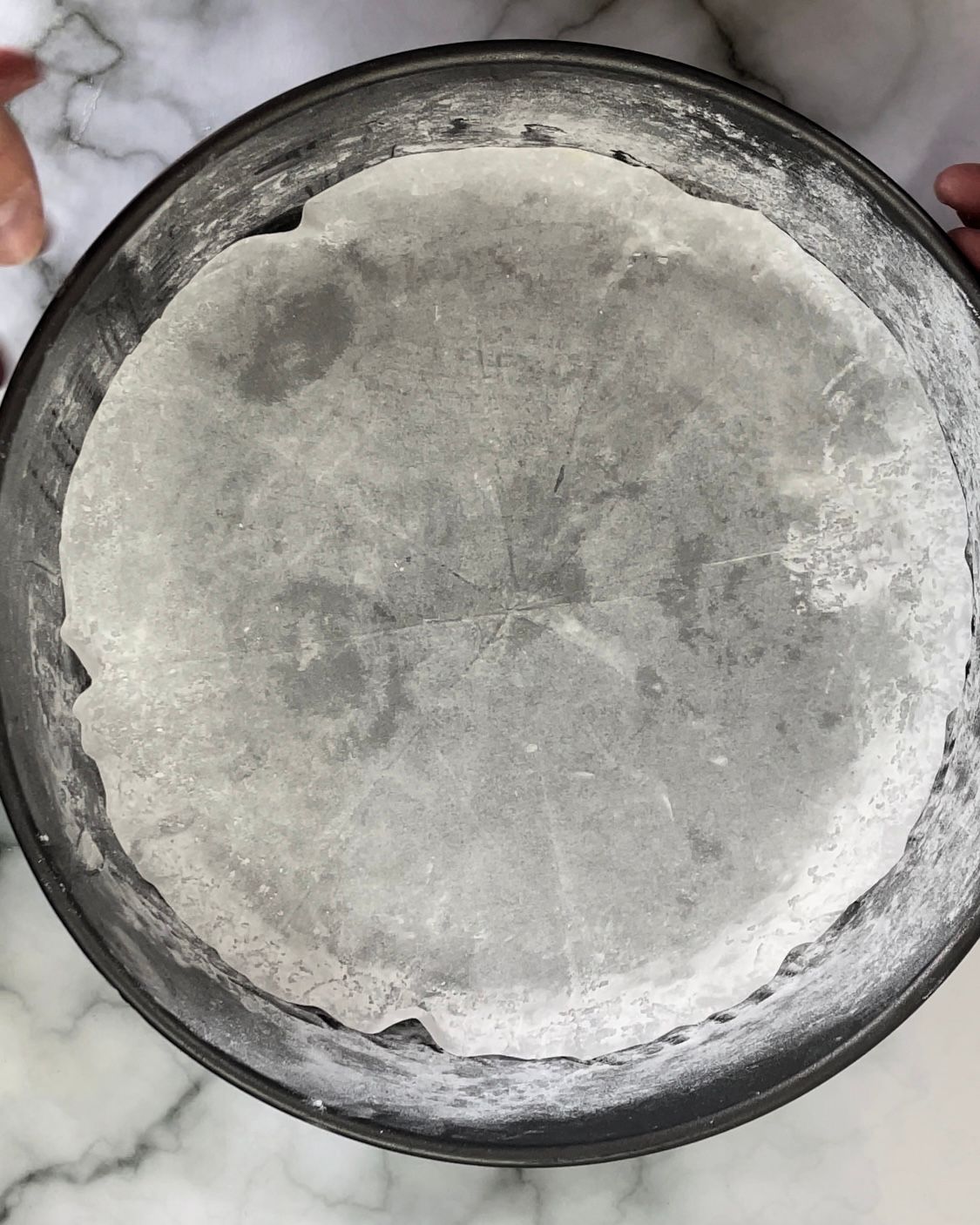 Una persona tiene in mano una padella piena di farina su un tavolo.