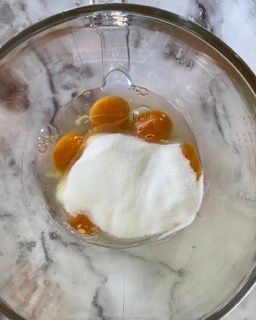 Una ciotola di vetro piena di uova e yogurt su un tavolo.