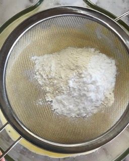 Una persona sta setacciando la farina in una ciotola piena di liquido.