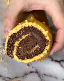 Una persona tiene in mano un rotolo di torta al cioccolato con un morso staccato