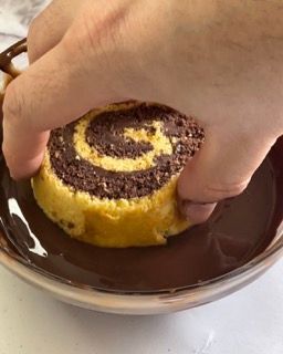 Una persona sta immergendo un rotolo di torta al cioccolato nella salsa al cioccolato