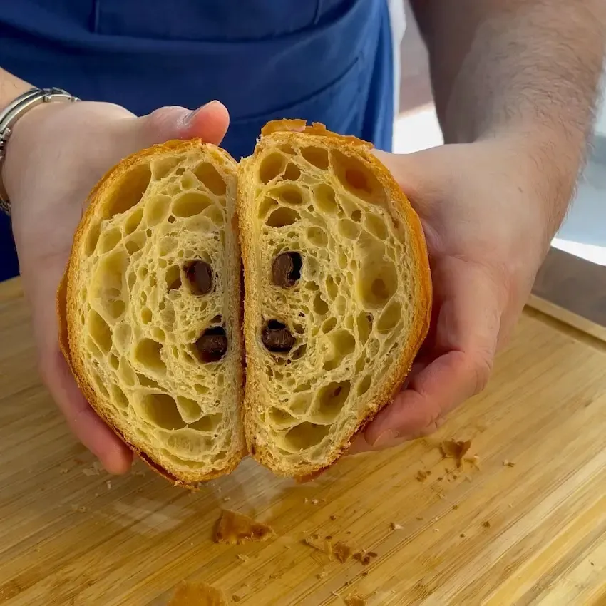 Primo piano di un pain au chocolat aperto che mostra la struttura interna a nido d'ape e il cuore di cioccolato fondente fuso.