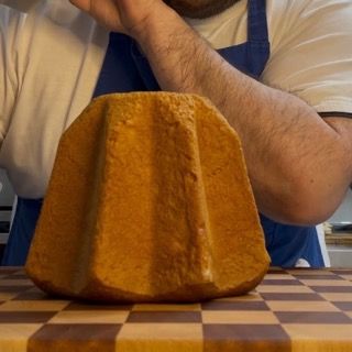 Un uomo con un grembiule tiene in mano un pezzo di pane su una tavola a scacchi