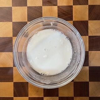 Una ciotola di vetro piena di liquido bianco su un tavolo a scacchi