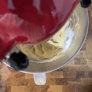 Una planetaria rossa sta mescolando un impasto in una ciotola di metallo su un tavolo di legno.