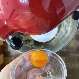 Una persona tiene in mano un bicchiere con un uovo dentro davanti a un mixer.