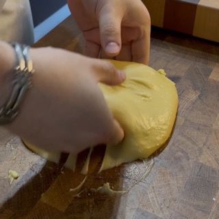 Una persona tiene in mano un pezzo di pasta su un tagliere.