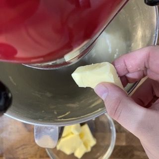 Una persona tiene in mano un pezzo di burro davanti a un mixer