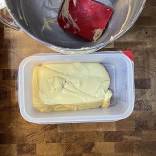 Un contenitore di plastica pieno di burro accanto a una ciotola di burro