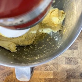 Un mixer sta mescolando un impasto in una ciotola di metallo su un tavolo di legno.