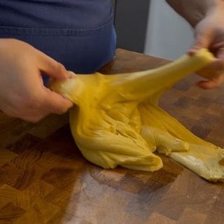 Una persona sta stendendo un pezzo di pasta su un tagliere