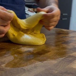 Una persona tiene in mano un pezzo di pasta gialla su un tagliere di legno.