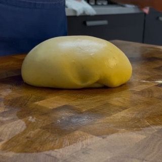 Una palla di pasta è appoggiata su un tagliere di legno.