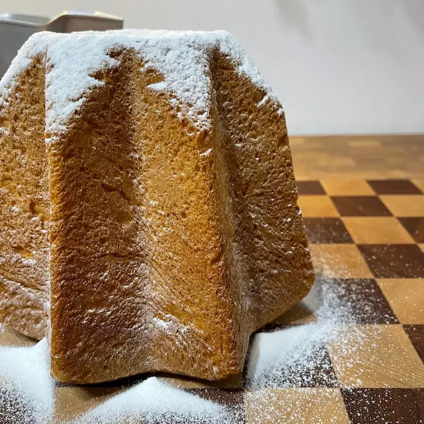 Pandoro fatto in casa con lievito di birra, alto e spolverato di zucchero a velo, forma a stella perfetta.