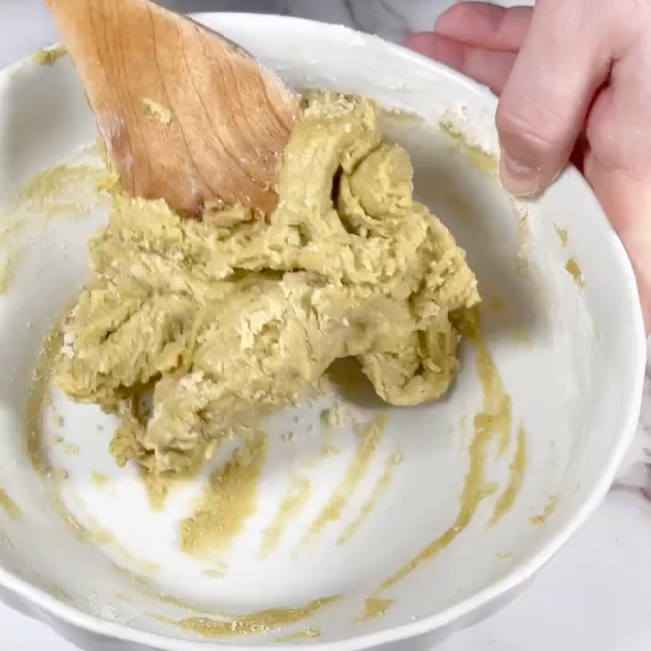 Una persona sta mescolando qualcosa in una ciotola con un cucchiaio di legno.