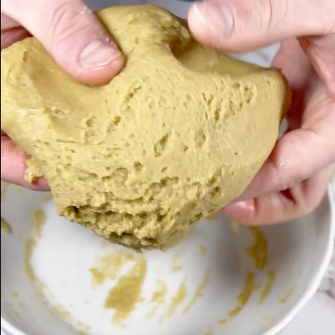 Una persona tiene un pezzo di impasto sopra una ciotola.