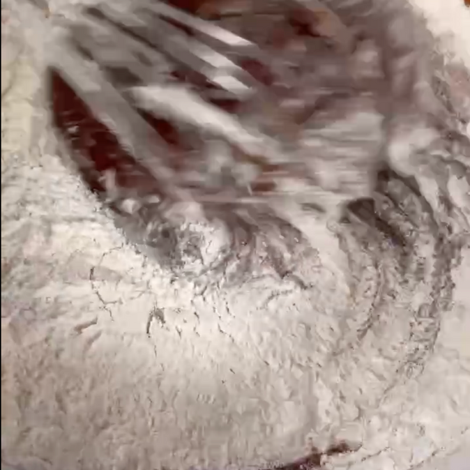 Una persona sta mescolando la farina in una ciotola con una frusta.