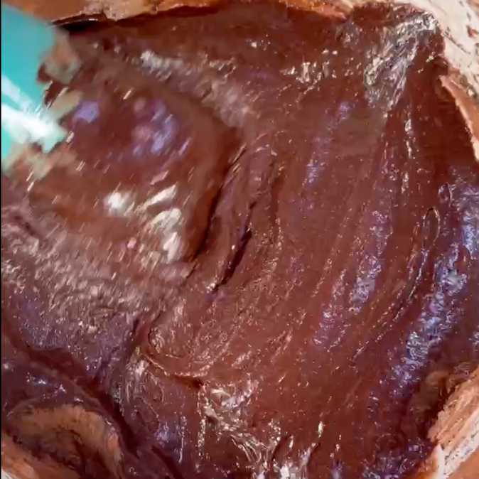 Primo piano di una ciotola di impasto al cioccolato con una spatola dentro.