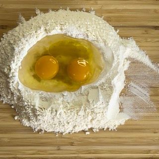 Due uova sono in un mucchio di farina su un tagliere di legno.