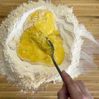 Una persona sta mescolando qualcosa in una ciotola di farina con una forchetta