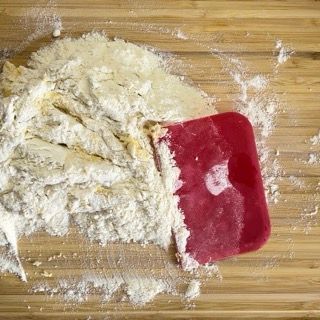 Una spatola rossa è appoggiata su un mucchio di farina su un tagliere di legno.