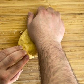 Una persona tiene in mano un pezzo di pasta su un tagliere di legno.