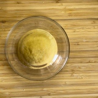 Una ciotola di vetro piena di una sostanza gialla è appoggiata su un tavolo di legno.