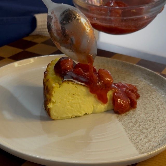 Cucchiaio che versa la composta di fragole sulla fetta di cheesecake.