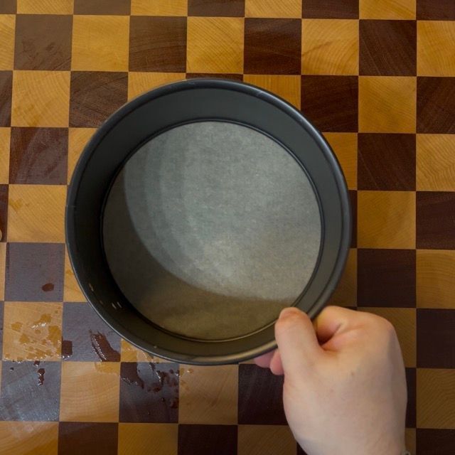 Mano che fa aderire la carta da forno umida a una teglia da 18cm