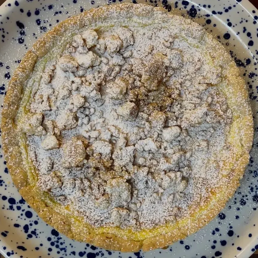 Cheesecake della nonna intera appena sfornata, ricoperta di pinoli tostati e zucchero a velo.