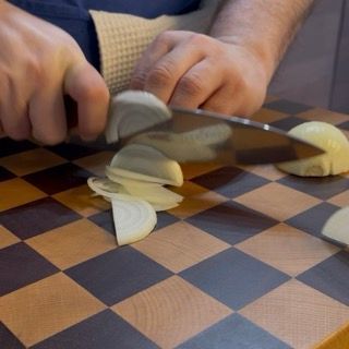 Taglio della cipolla a fettine sottili per la base della salsa dei conchiglioni ripieni.