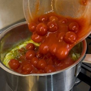 Aggiunta dei pomodori datterini in conserva per una conchiglioni ripieni ricetta gourmet.