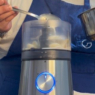 Aggiunta di due cucchiai di latte di cottura caldo nel mixer per la crema di aglio per pasta.