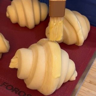 Croissant francesi lievitati in teglia spennellati con uovo e panna prima della cottura