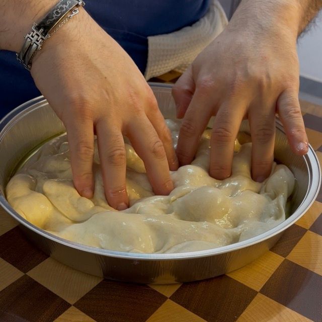 Mani che stendono l'impasto della focaccia su tutta la teglia