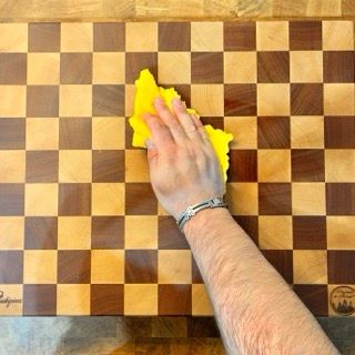 Una persona sta pulendo un tagliere di legno con un panno giallo