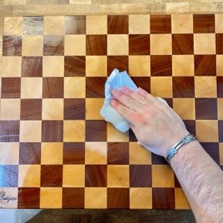 Una persona sta pulendo un tagliere di legno con un panno