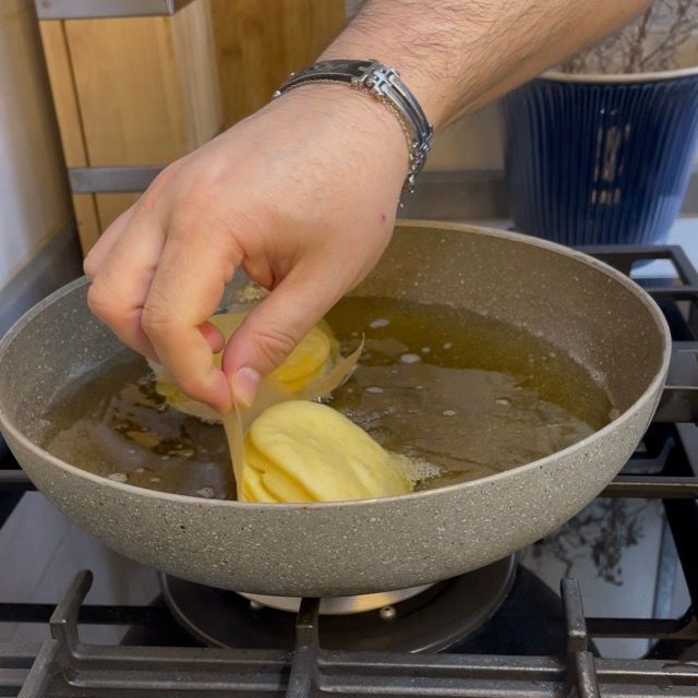 Krapfen che scivola nell'olio caldo con il suo quadrato di carta forno.