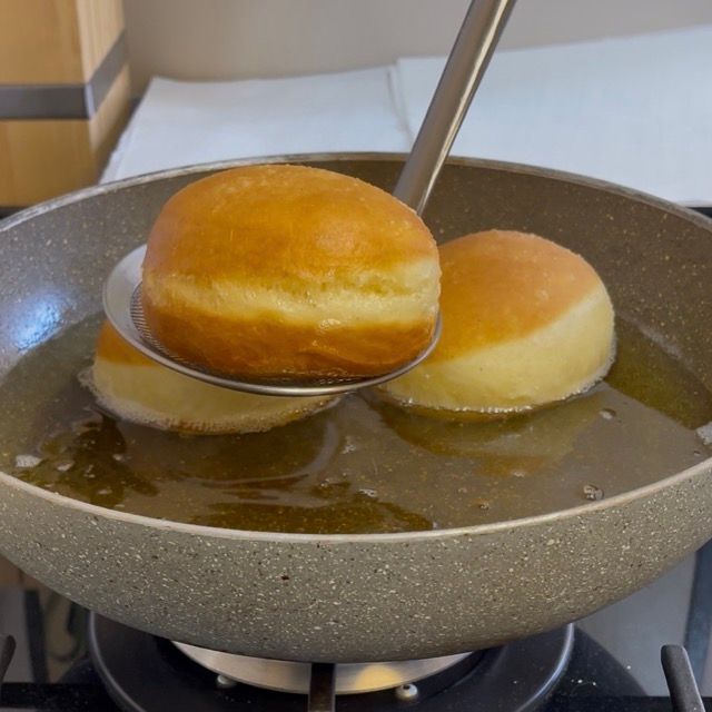 Schiumarola che preleva i bomboloni cotti e dorati dall'olio.